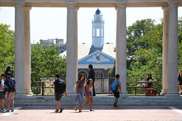 Students walk past columns on a sun-drenched campus quad